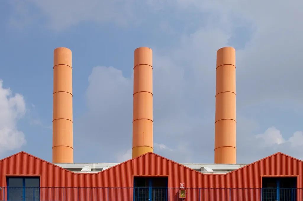 Three tall chimneys rise from a red-roofed building