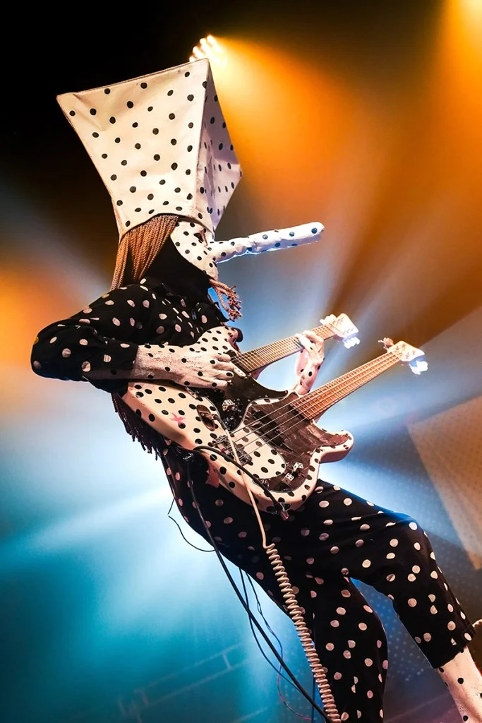 music performer in black and white spotted mask against orange and blue lights