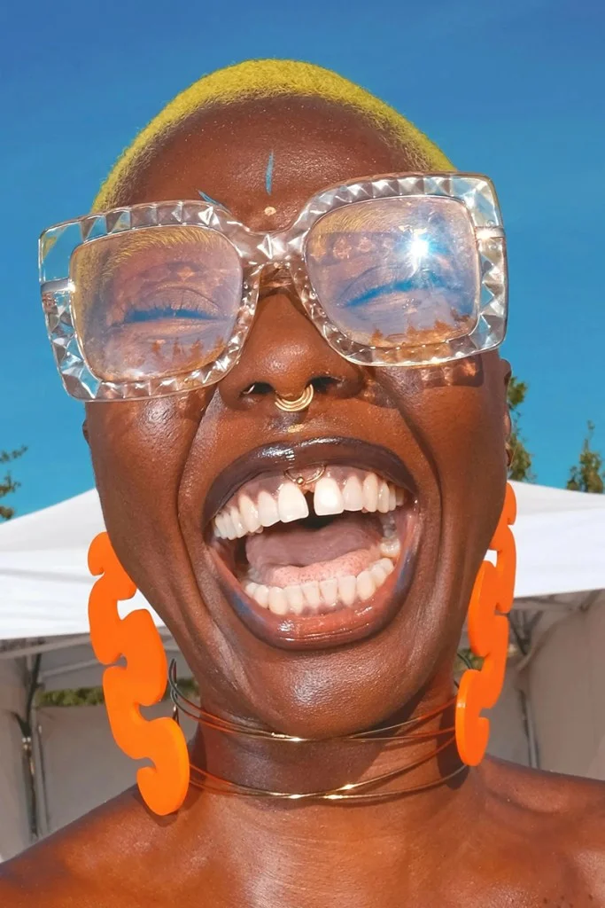 close-up photo of a woman laughing wearing funky sunglasses and bright orange earrings