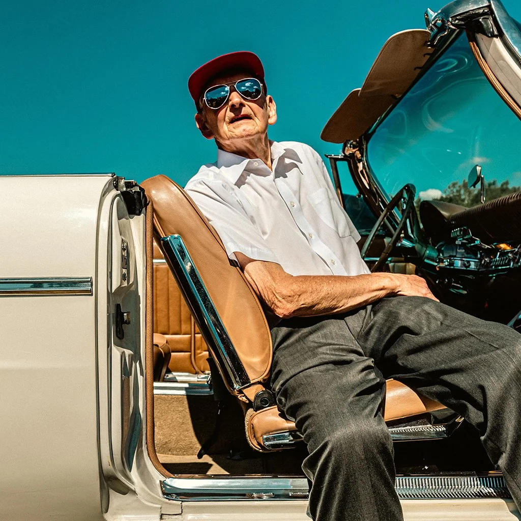 portrait of an older man in baseball cap sat in vintage american car