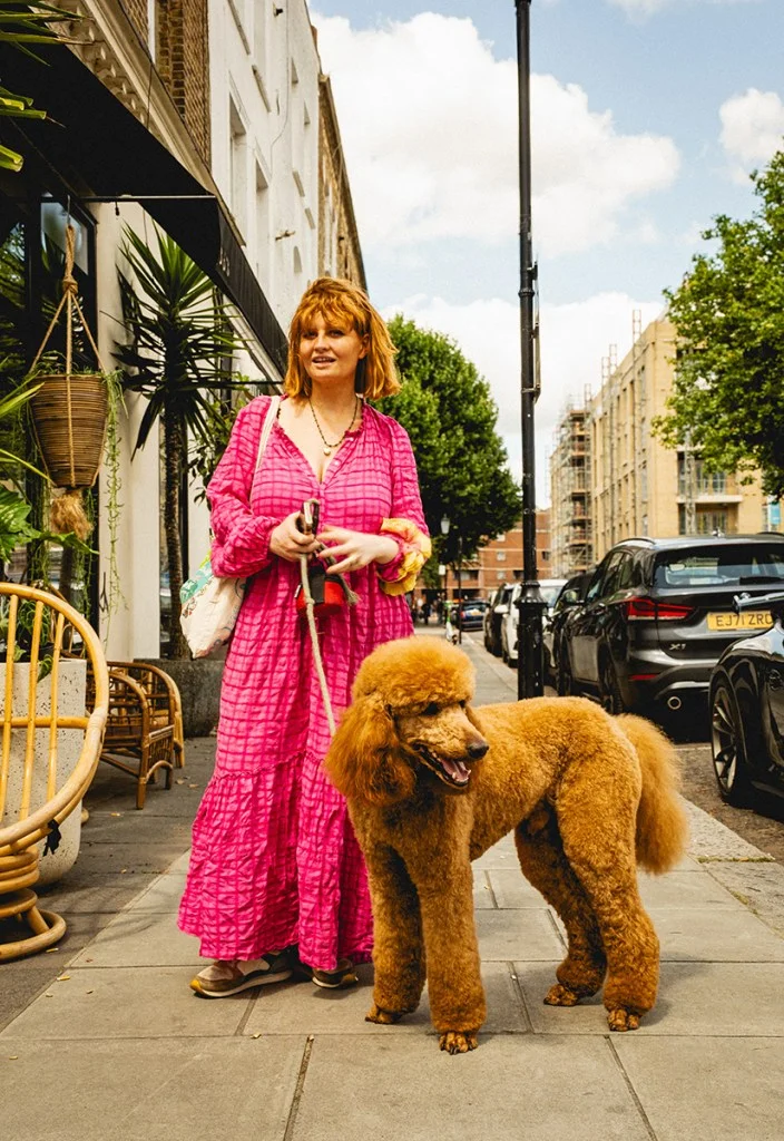 woman in pink stood next to brown tan poodle