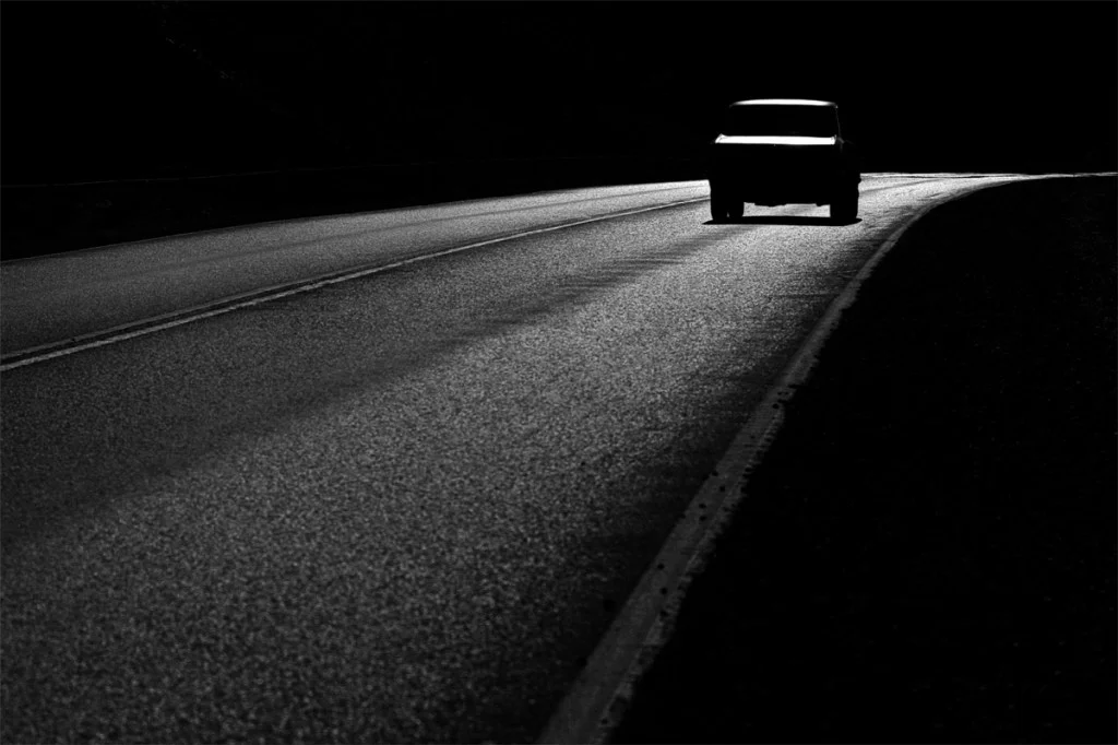 black and white photo of a car driving on the road