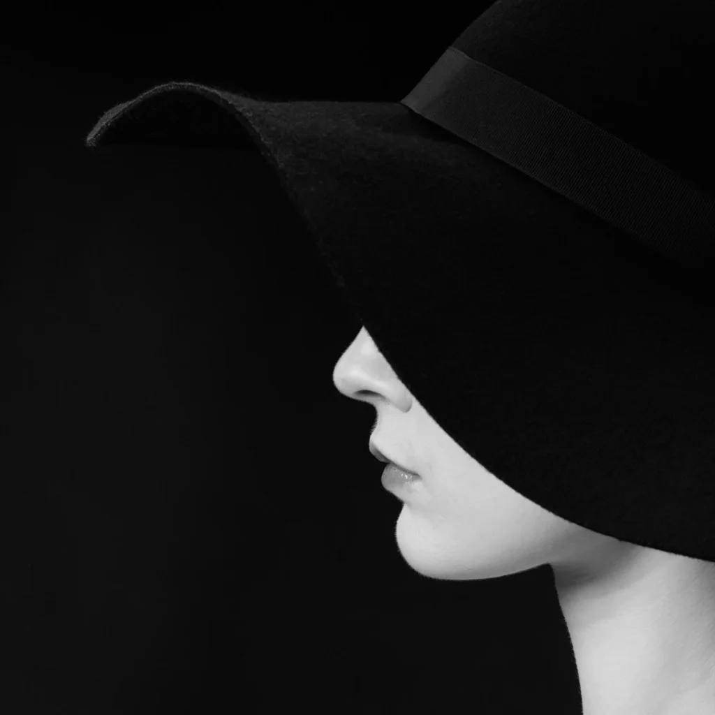 side profile of a woman wearing a large black hat that covers half her face