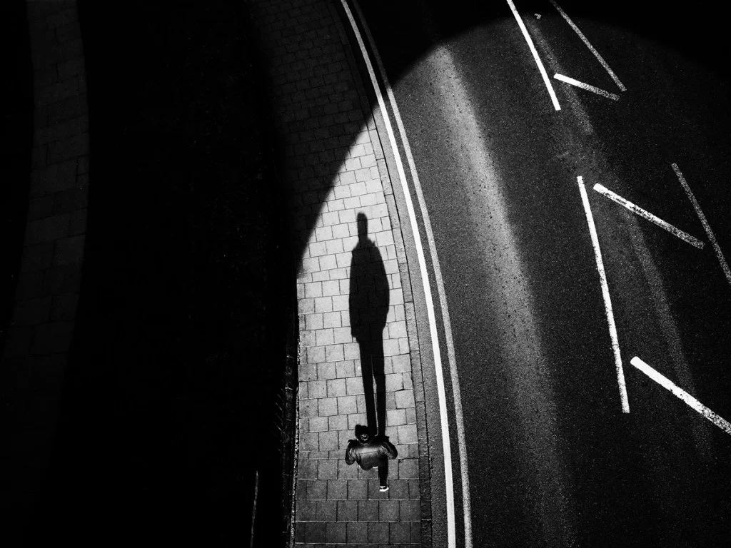black and white photo looking down on someone walking with a long shadow cast ahead of them