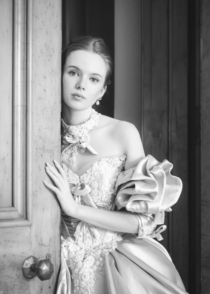 black and white photo of a woman in a large ball gown leaning against a door