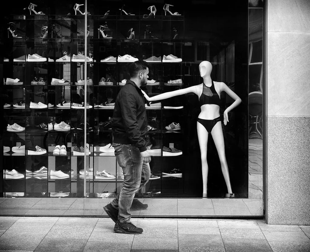 A person walking past a shop with a mannequin in the window