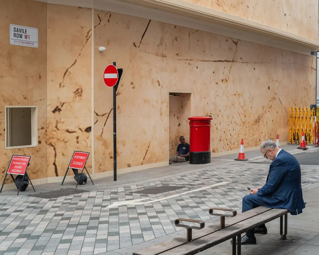 Photo of two people sat on a bench looking at phones