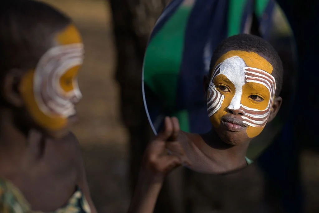 Child with face paint holding a mirror