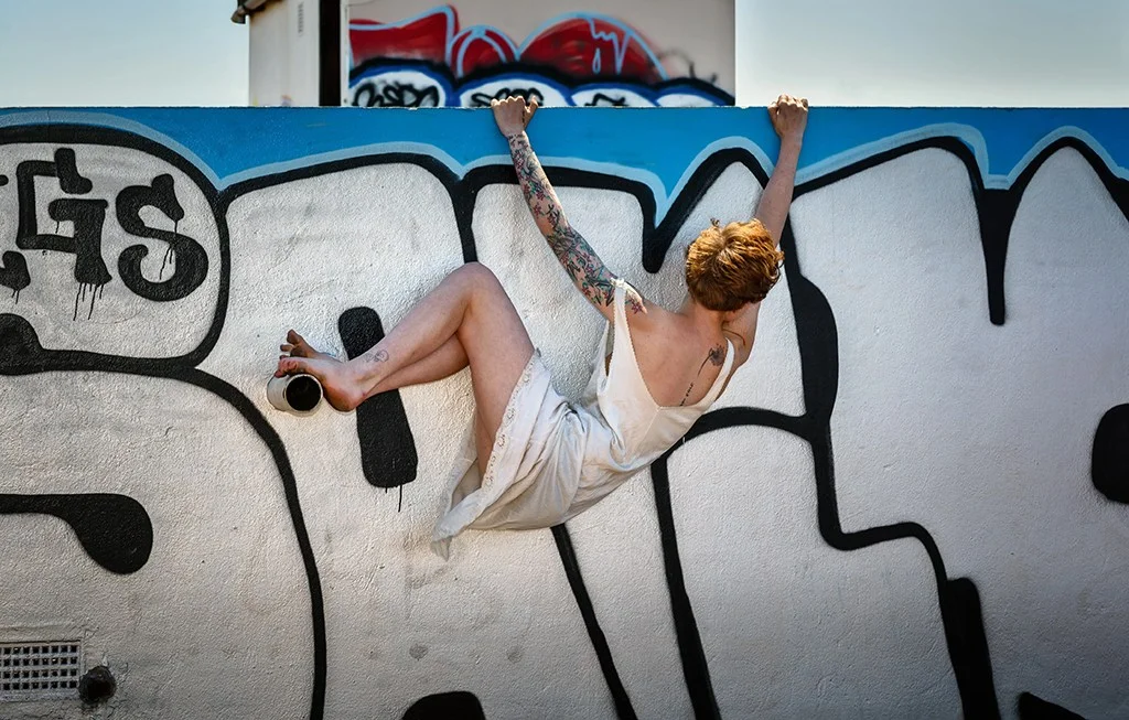 woman in white dress holding onto graffiti wall
