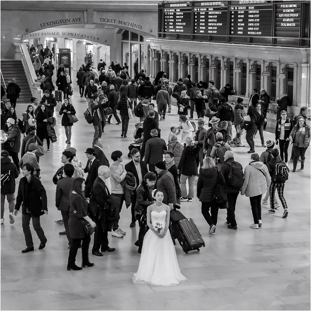 busy crowd in a train station with a bride in white dress amongst