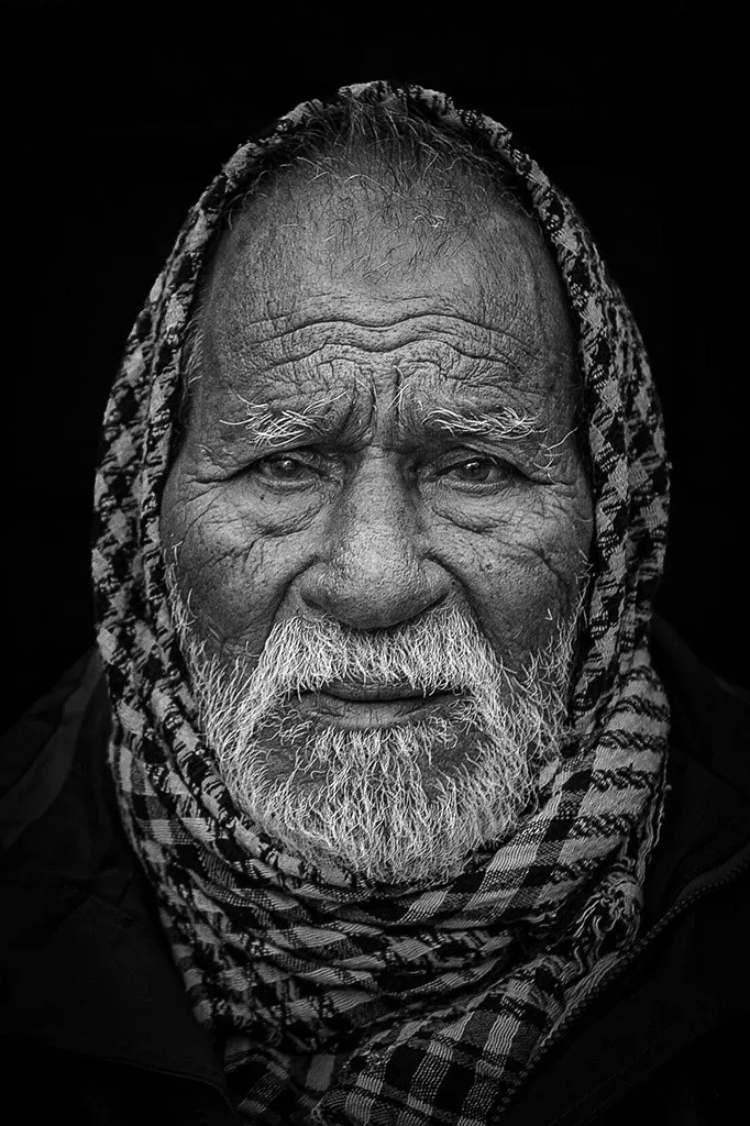 close-up black & white portrait of a man wearing a check scarf around his head