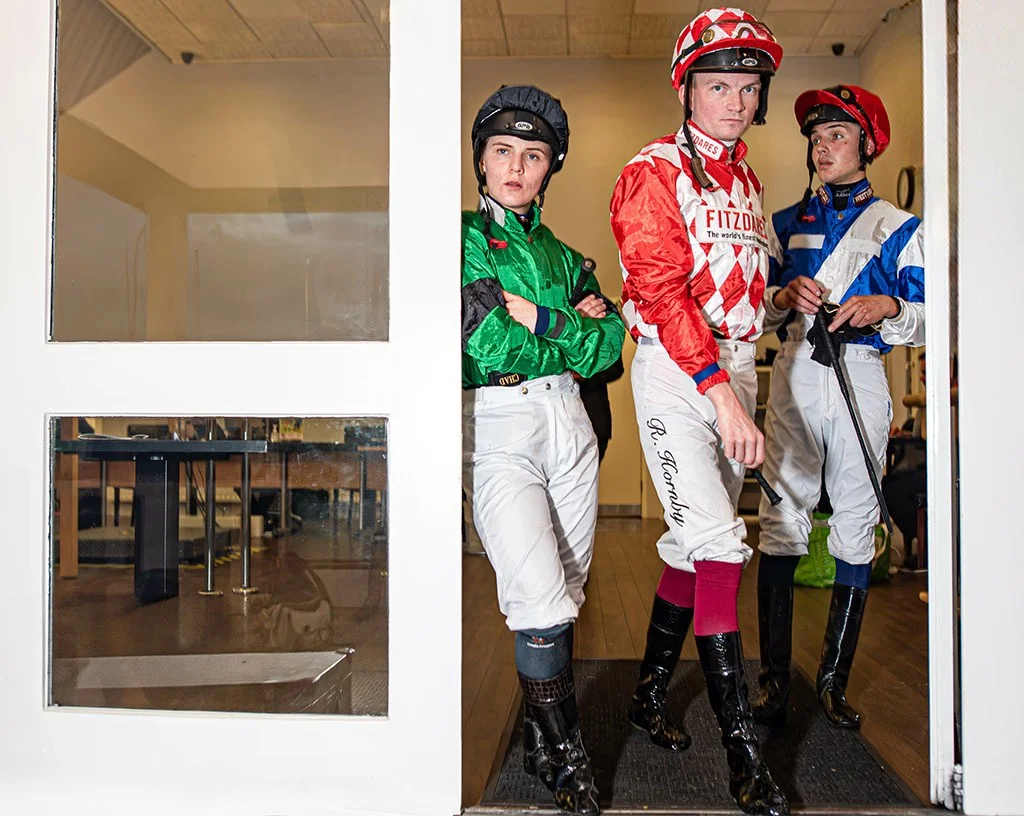 portrait of three jockeys in bright colours stood in a doorway