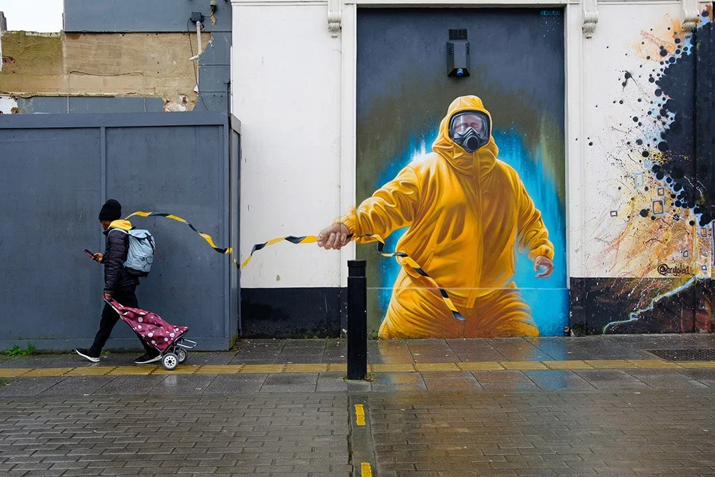 winner of the apoy urban life 2024 round image of person walking past street art with black and yellow tape 